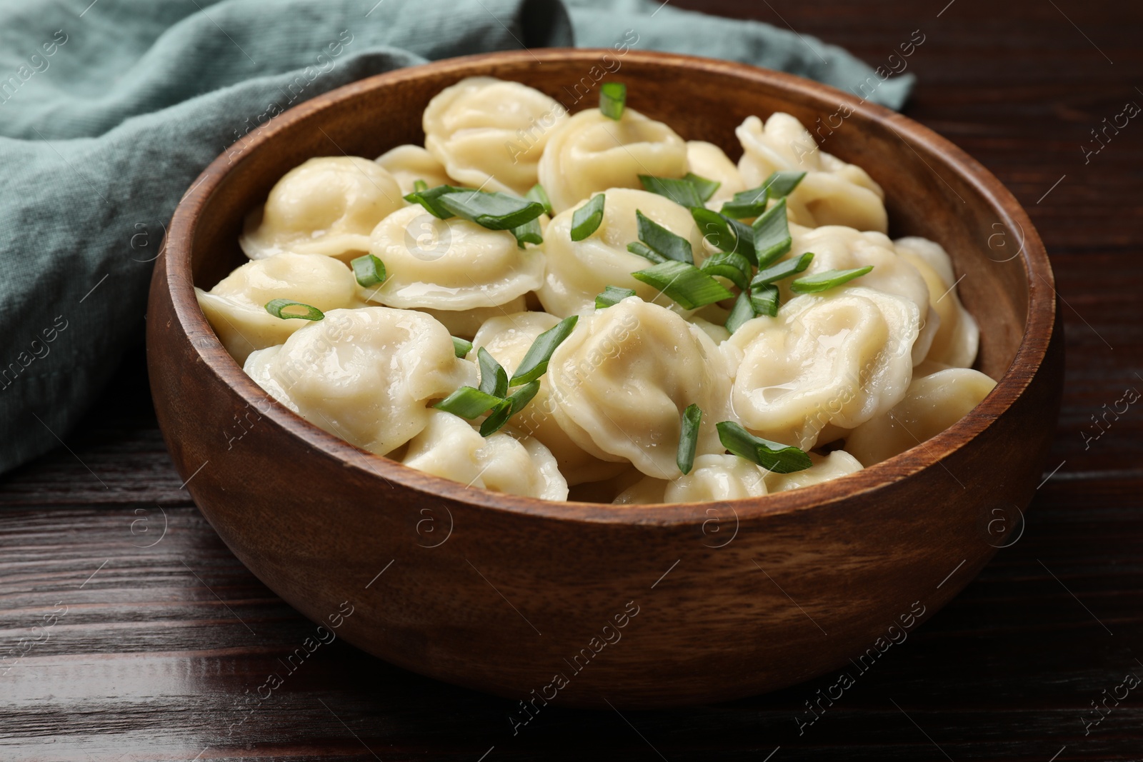 Photo of Delicious pelmeni with green onion in bowl on wooden table, closeup