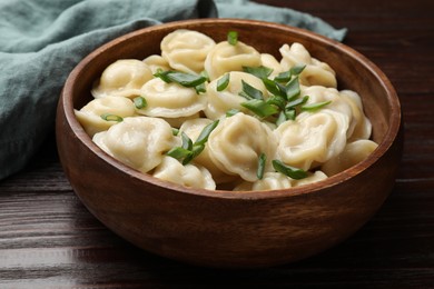 Photo of Delicious pelmeni with green onion in bowl on wooden table, closeup