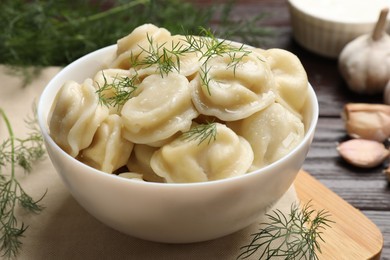 Photo of Delicious pelmeni with dill served on wooden table, closeup