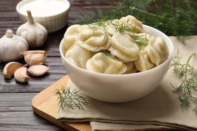 Photo of Delicious pelmeni with dill served on wooden table, closeup