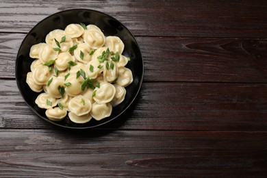 Photo of Delicious pelmeni with green onion in bowl on wooden table, top view. Space for text