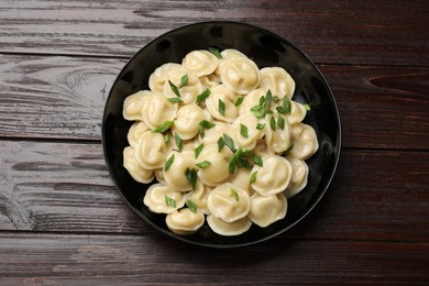 Photo of Delicious pelmeni with green onion in bowl on wooden table, top view