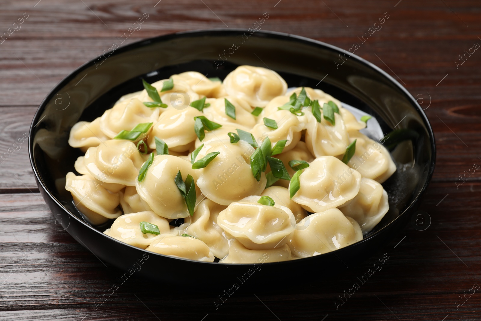 Photo of Delicious pelmeni with green onion in bowl on wooden table, closeup