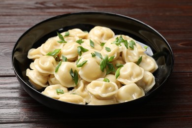 Photo of Delicious pelmeni with green onion in bowl on wooden table, closeup