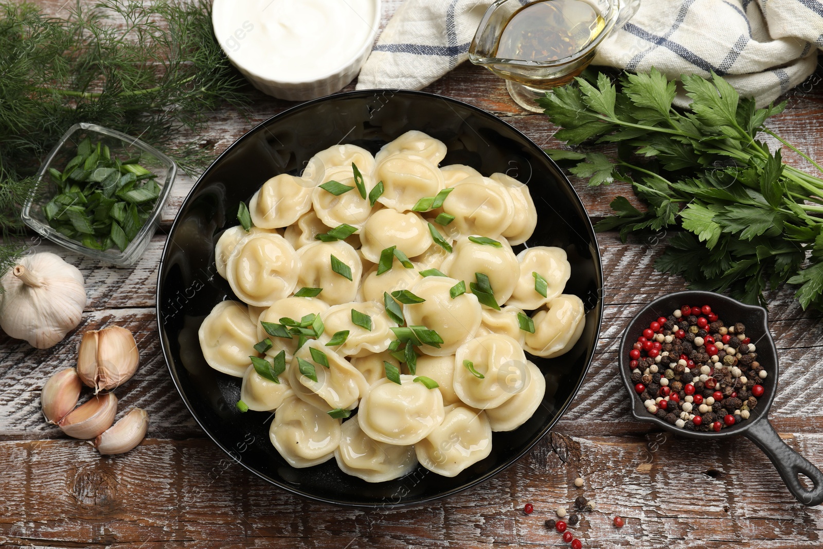 Photo of Delicious pelmeni with green onion served on wooden table, flat lay