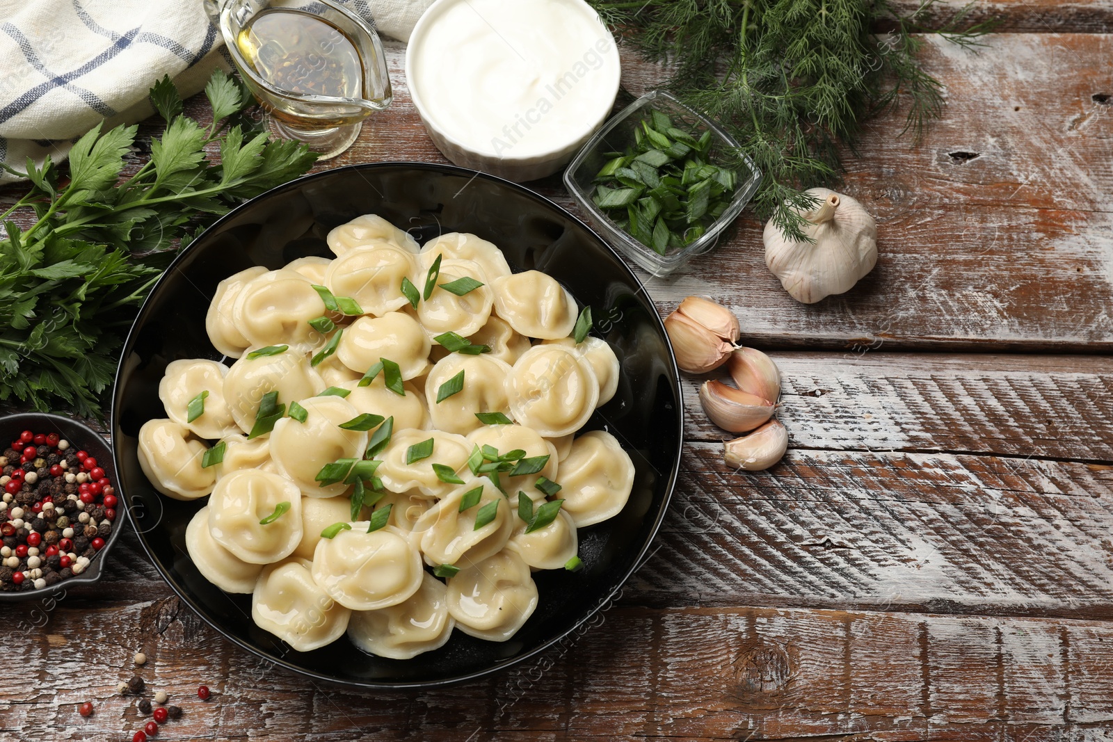 Photo of Delicious pelmeni with green onion served on wooden table, flat lay