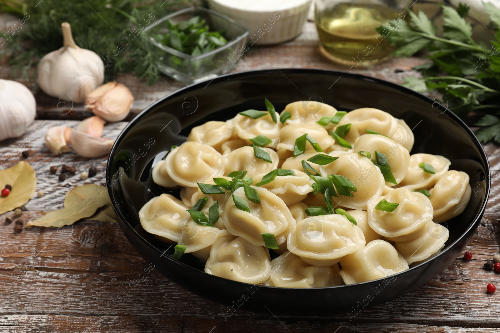 Photo of Delicious pelmeni with green onion served on wooden table, closeup