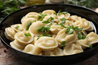 Photo of Delicious pelmeni with green onion in bowl on wooden table, closeup