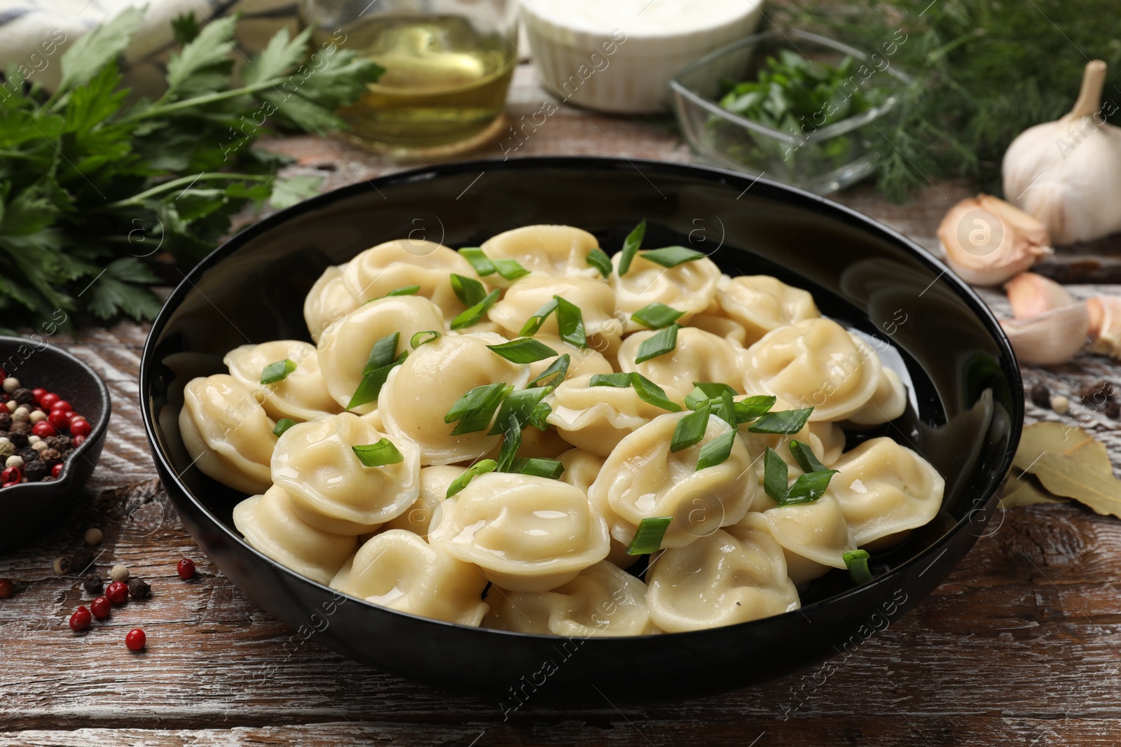 Photo of Delicious pelmeni with green onion served on wooden table, closeup