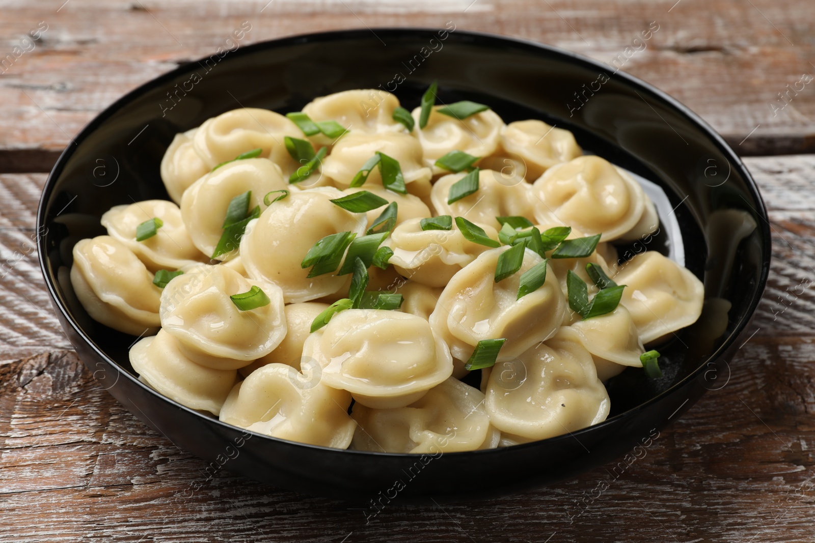 Photo of Delicious pelmeni with green onion in bowl on wooden table, closeup