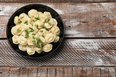 Photo of Delicious pelmeni with green onion in bowl on wooden table, top view. Space for text