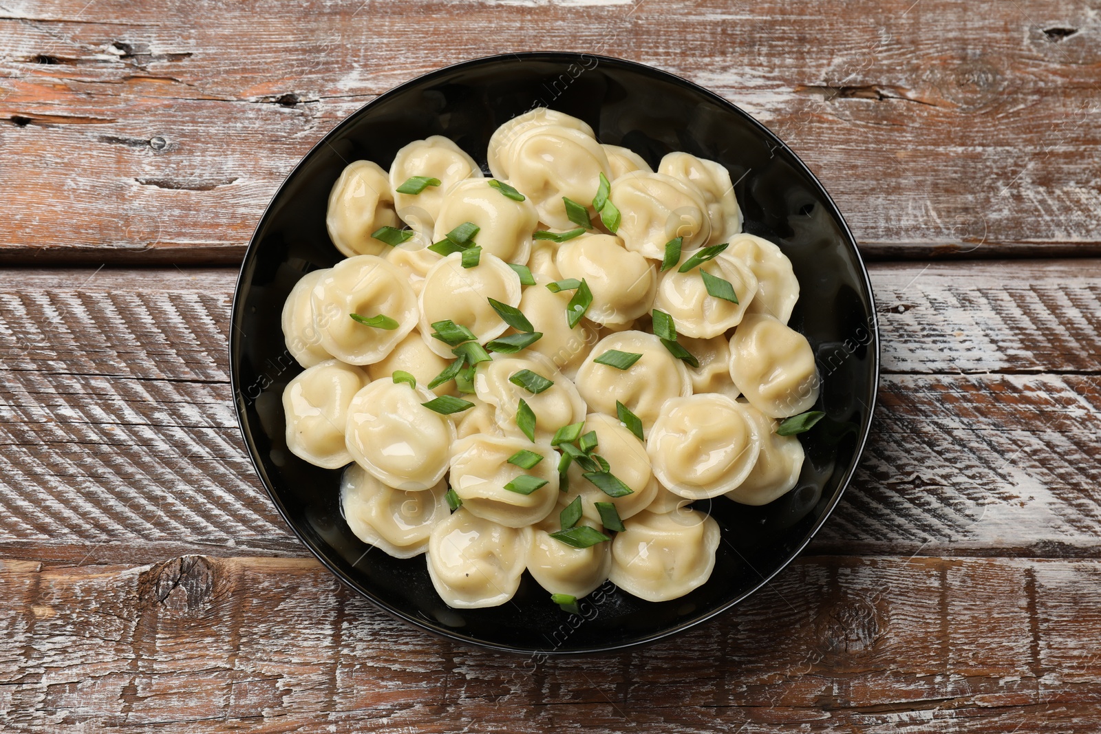 Photo of Delicious pelmeni with green onion in bowl on wooden table, top view