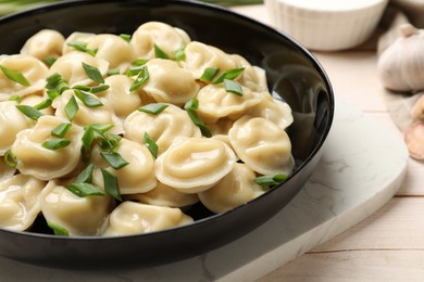 Photo of Delicious pelmeni with green onion in bowl on wooden table, closeup