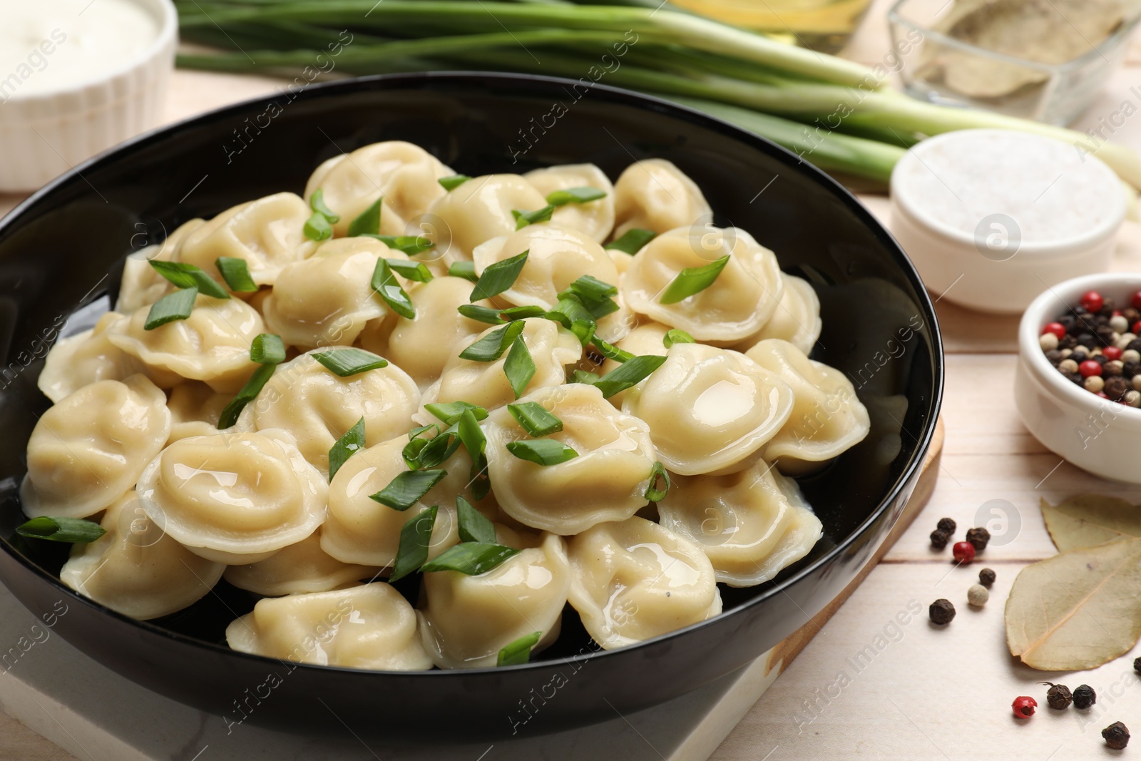 Photo of Delicious pelmeni with green onion served on wooden table, closeup