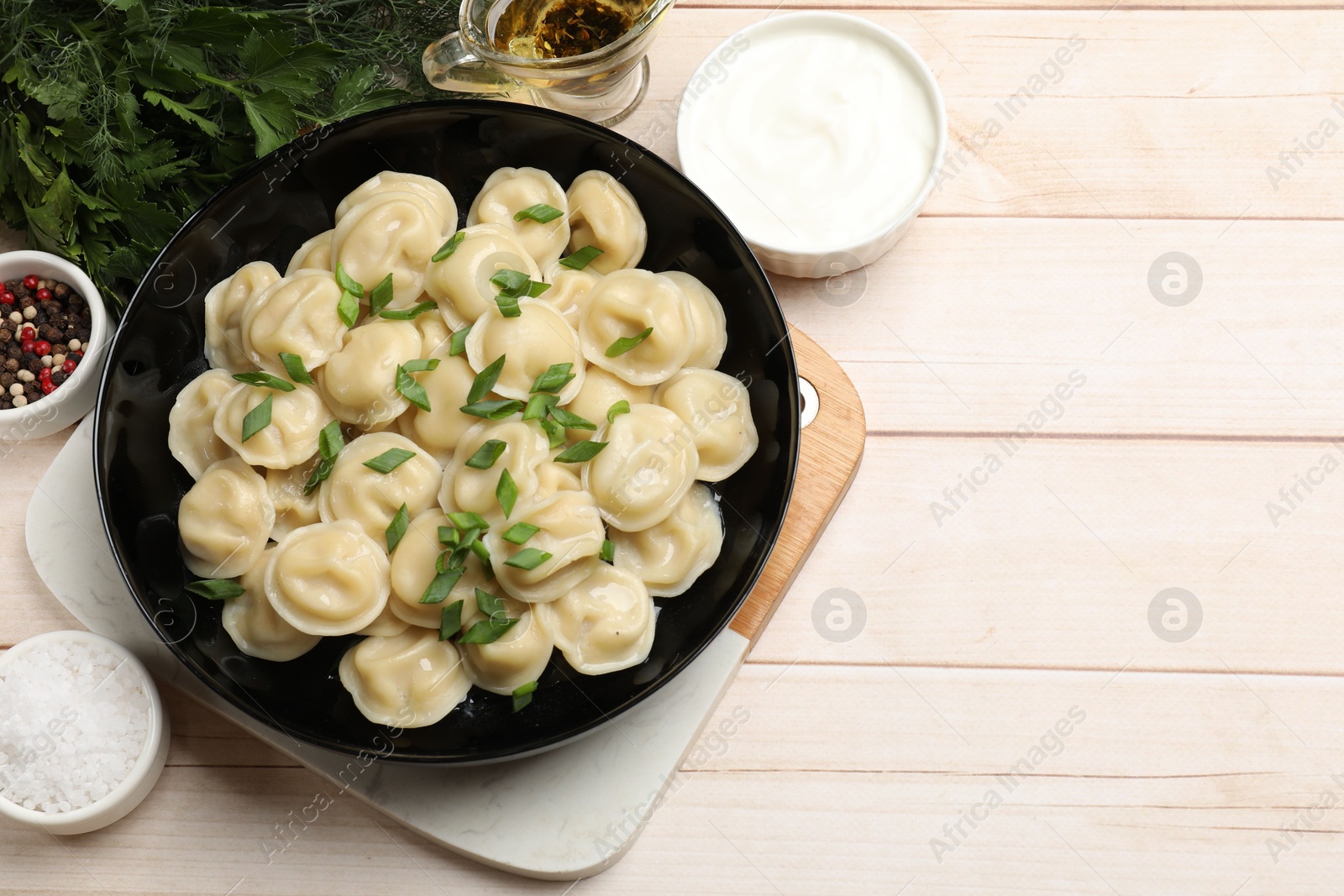 Photo of Delicious pelmeni with green onion served on wooden table, flat lay. Space for text