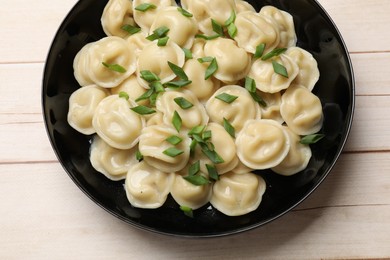 Photo of Delicious pelmeni with green onion in bowl on wooden table, top view