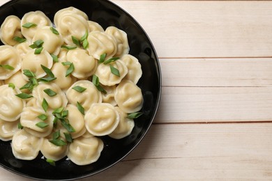 Photo of Delicious pelmeni with green onion in bowl on wooden table, top view. Space for text