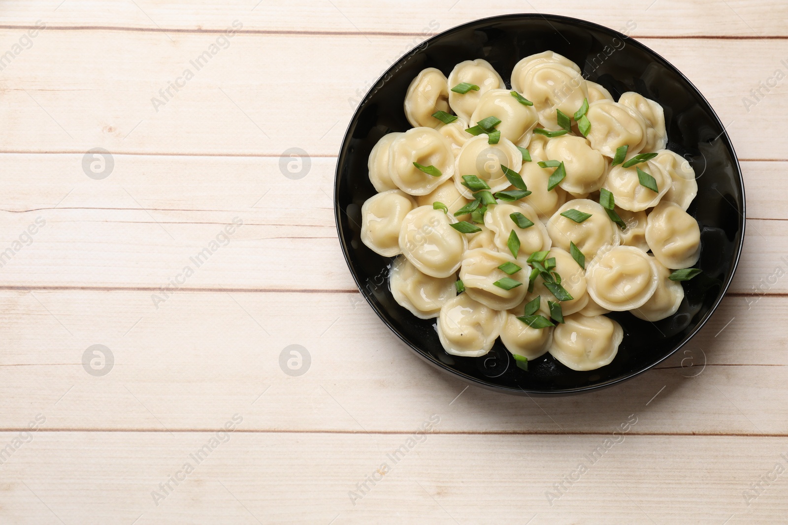 Photo of Delicious pelmeni with green onion in bowl on wooden table, top view. Space for text