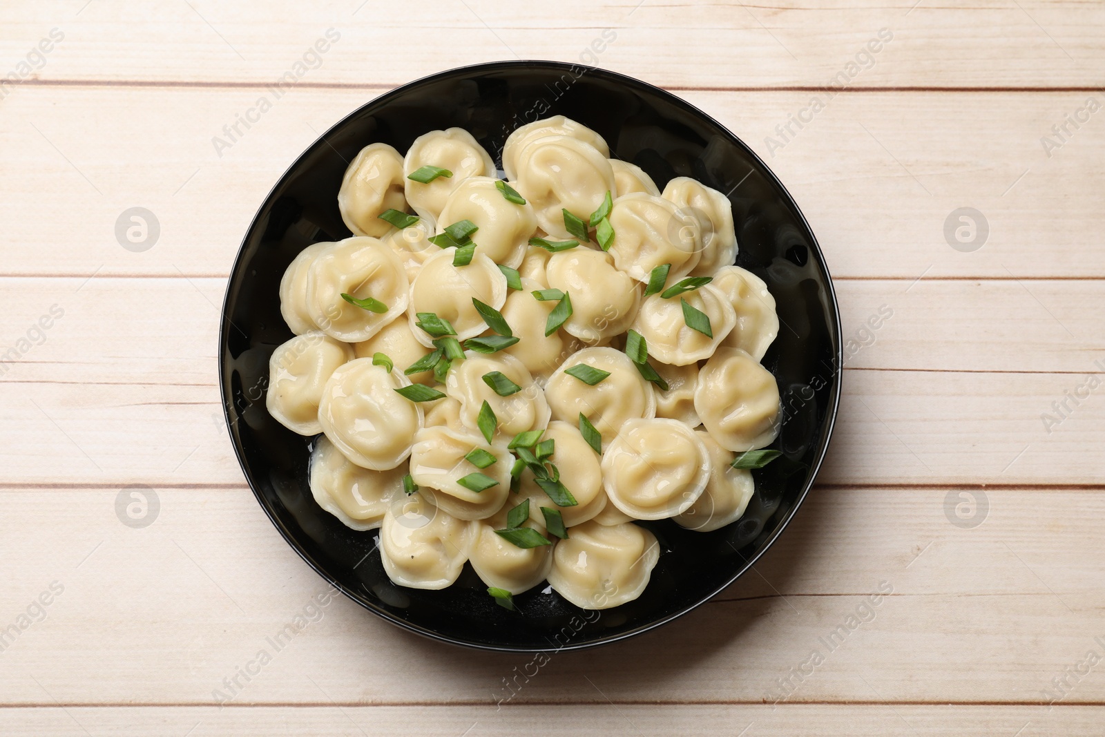 Photo of Delicious pelmeni with green onion in bowl on wooden table, top view