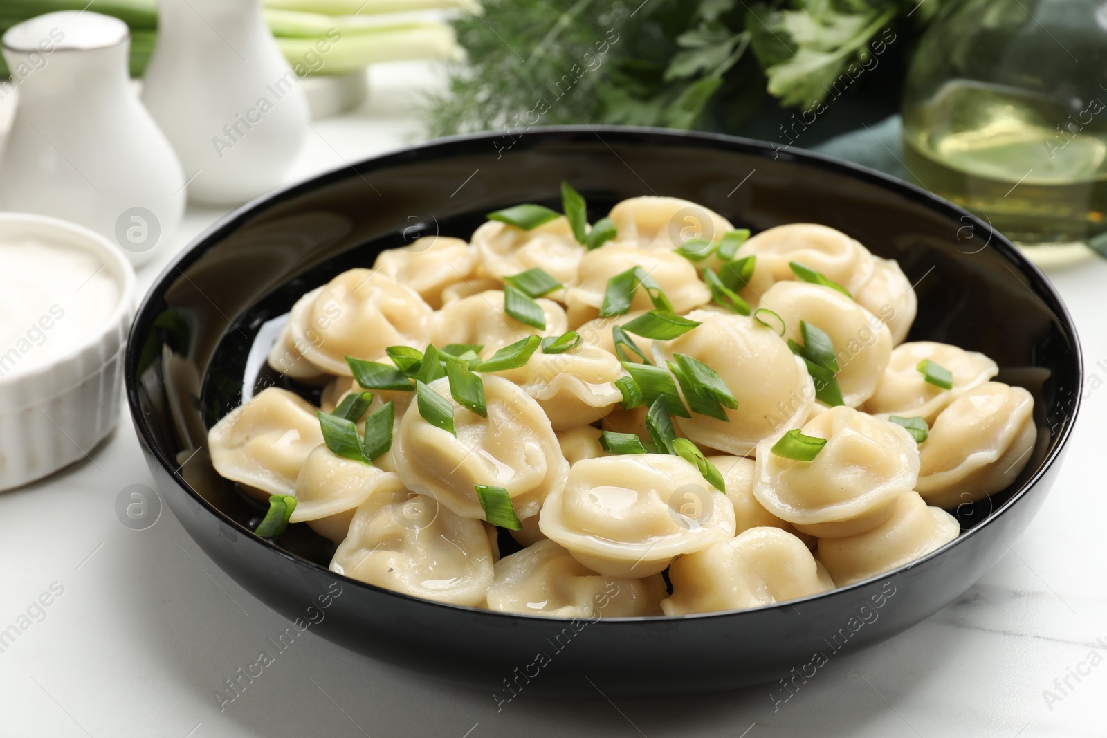 Photo of Delicious pelmeni with green onion served on light table, closeup