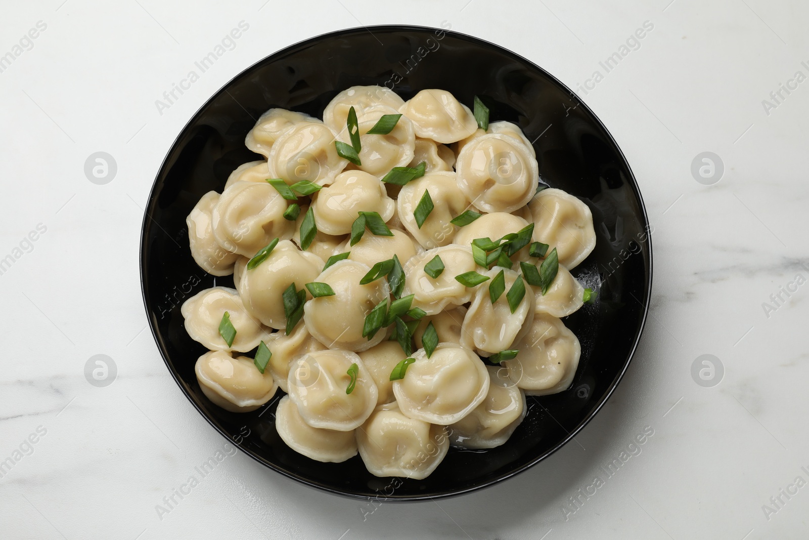 Photo of Delicious pelmeni with green onion in bowl on light table, top view