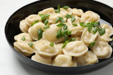 Photo of Delicious pelmeni with green onion in bowl on light table, closeup