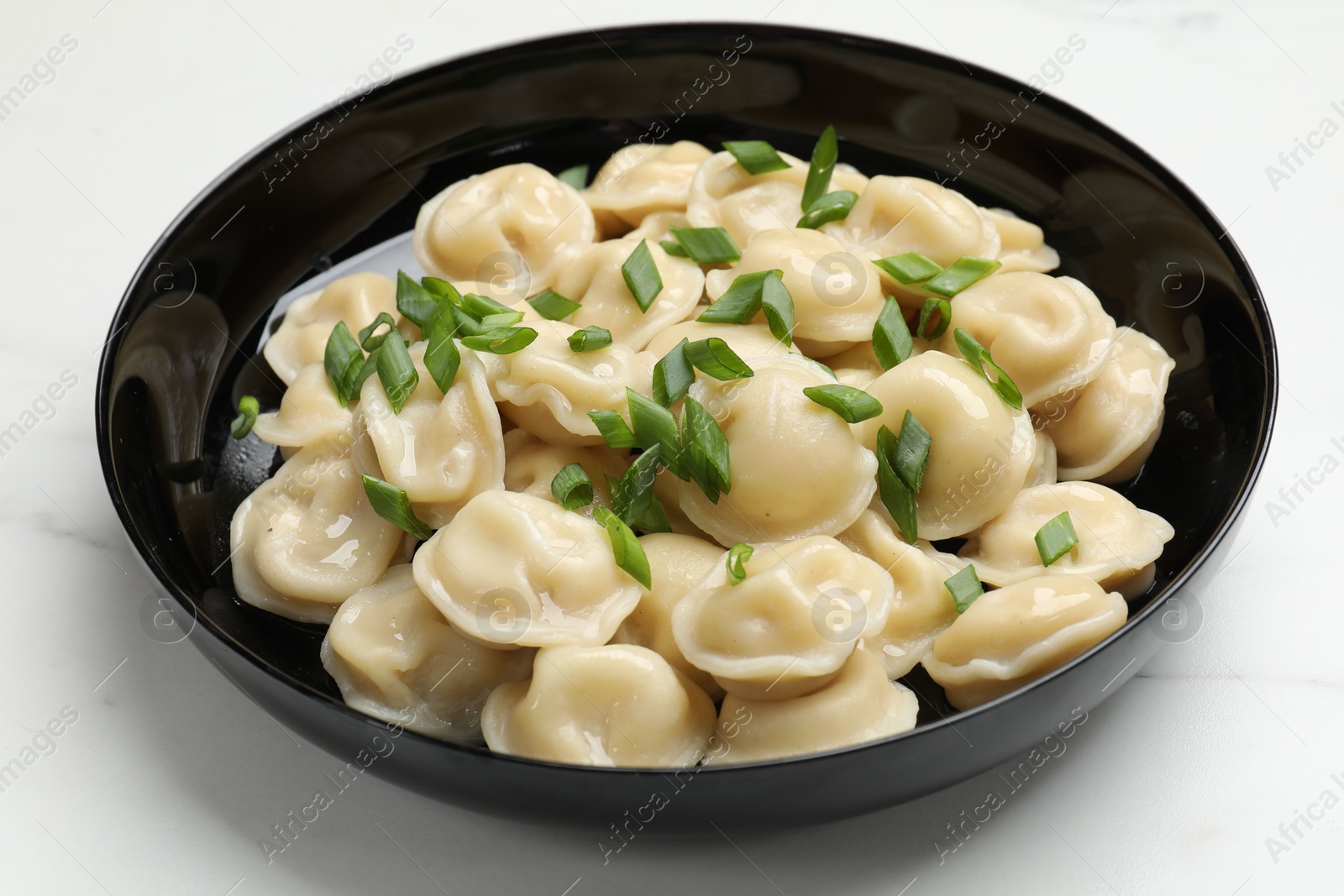 Photo of Delicious pelmeni with green onion in bowl on light table, closeup