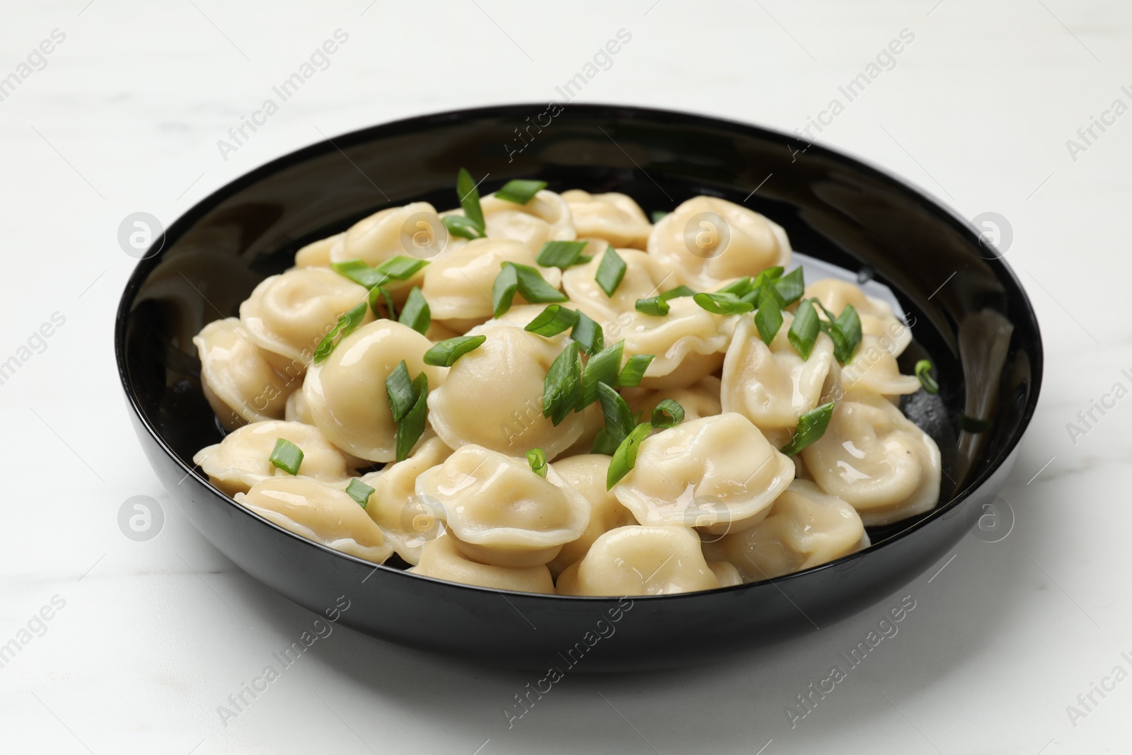 Photo of Delicious pelmeni with green onion in bowl on light table, closeup