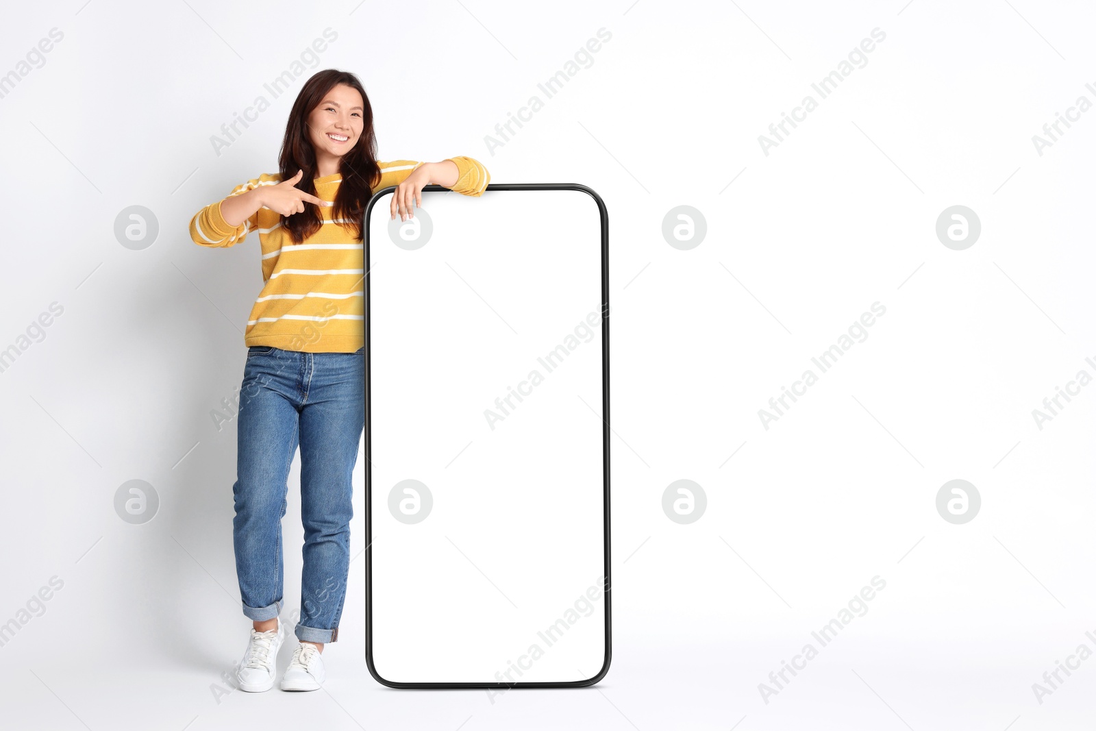 Image of Happy smiling woman pointing at big mobile phone with blank screen on white background. Mockup for design