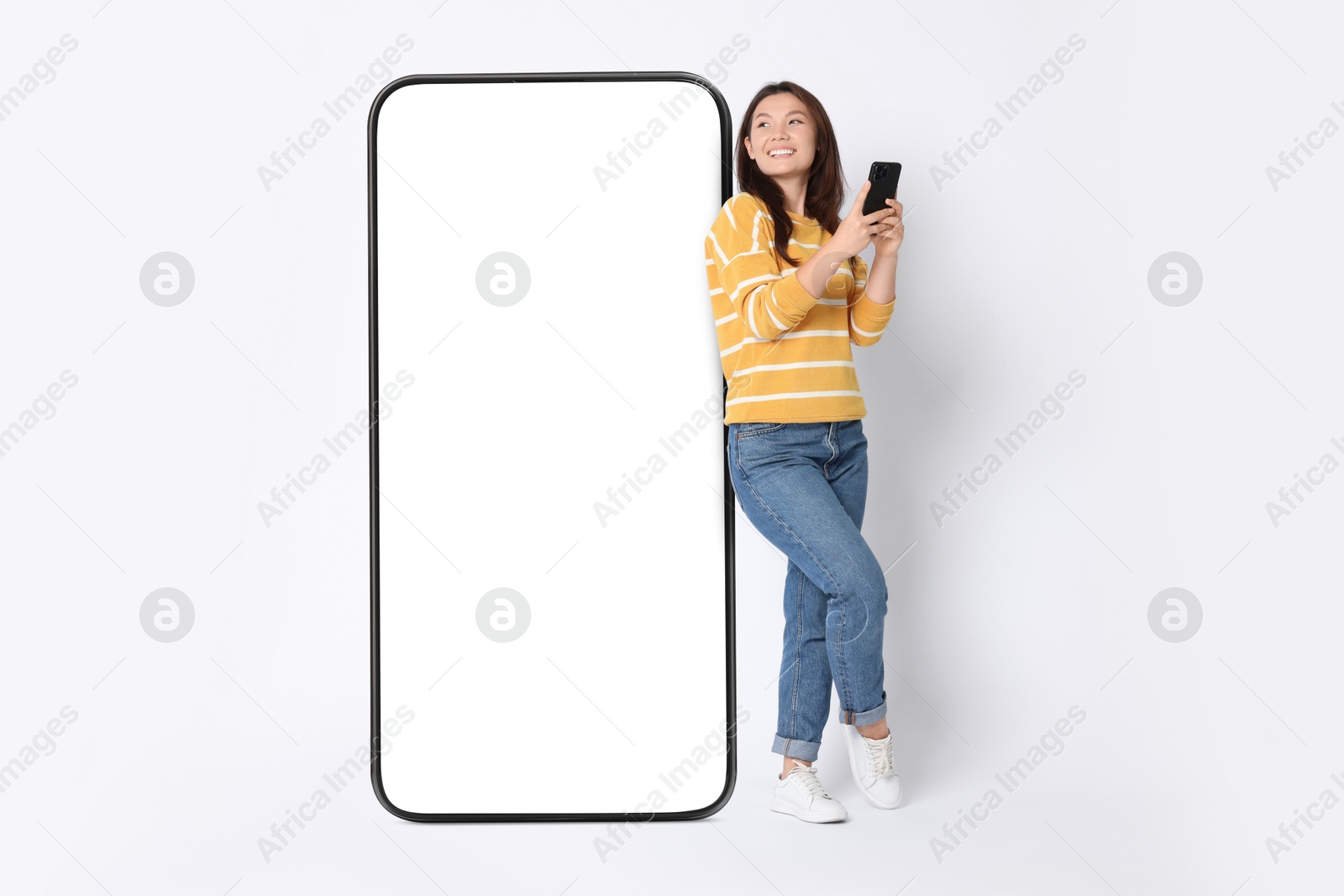 Image of Happy smiling woman with smartphone standing near big mobile phone with blank screen on white background. Mockup for design