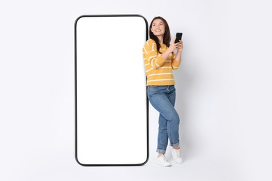 Image of Happy smiling woman with smartphone standing near big mobile phone with blank screen on white background. Mockup for design