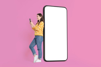 Image of Happy smiling woman using smartphone while standing near big mobile phone with blank screen on color background. Mockup for design