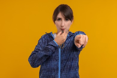 Young woman blowing whistle on orange background