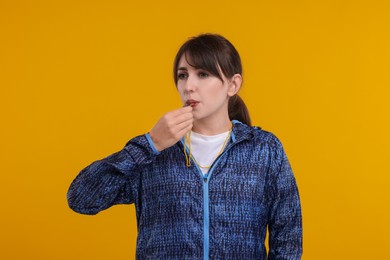 Photo of Young woman blowing whistle on orange background