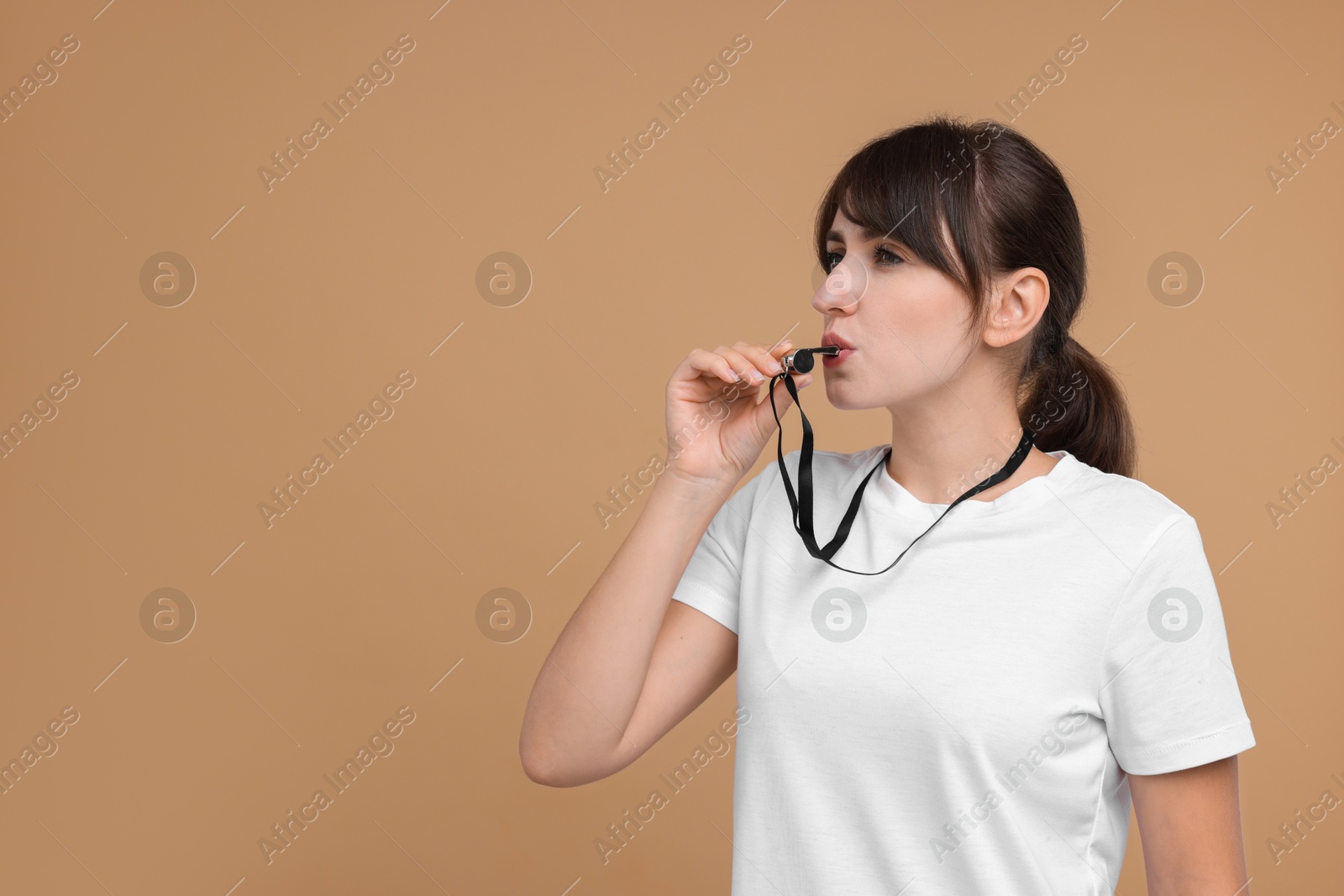 Photo of Woman blowing whistle on beige background, space for text