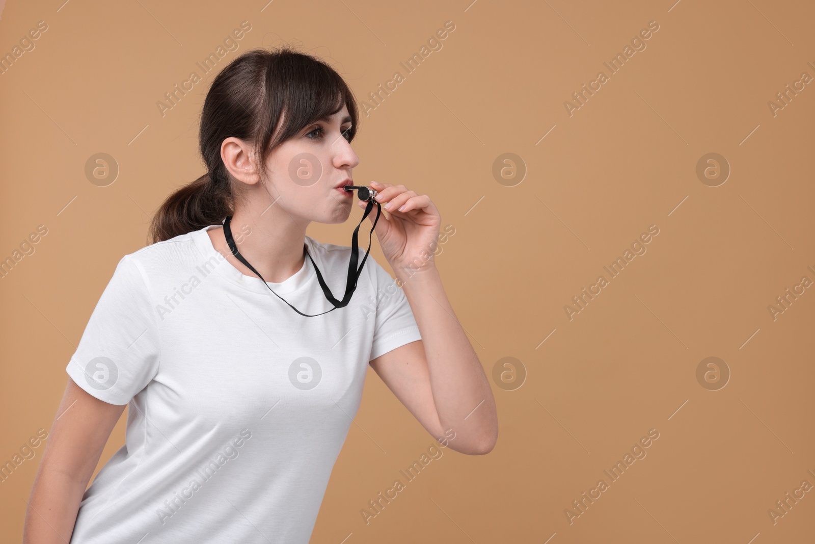 Photo of Woman blowing whistle on beige background, space for text