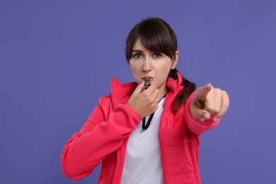 Young woman blowing whistle on purple background