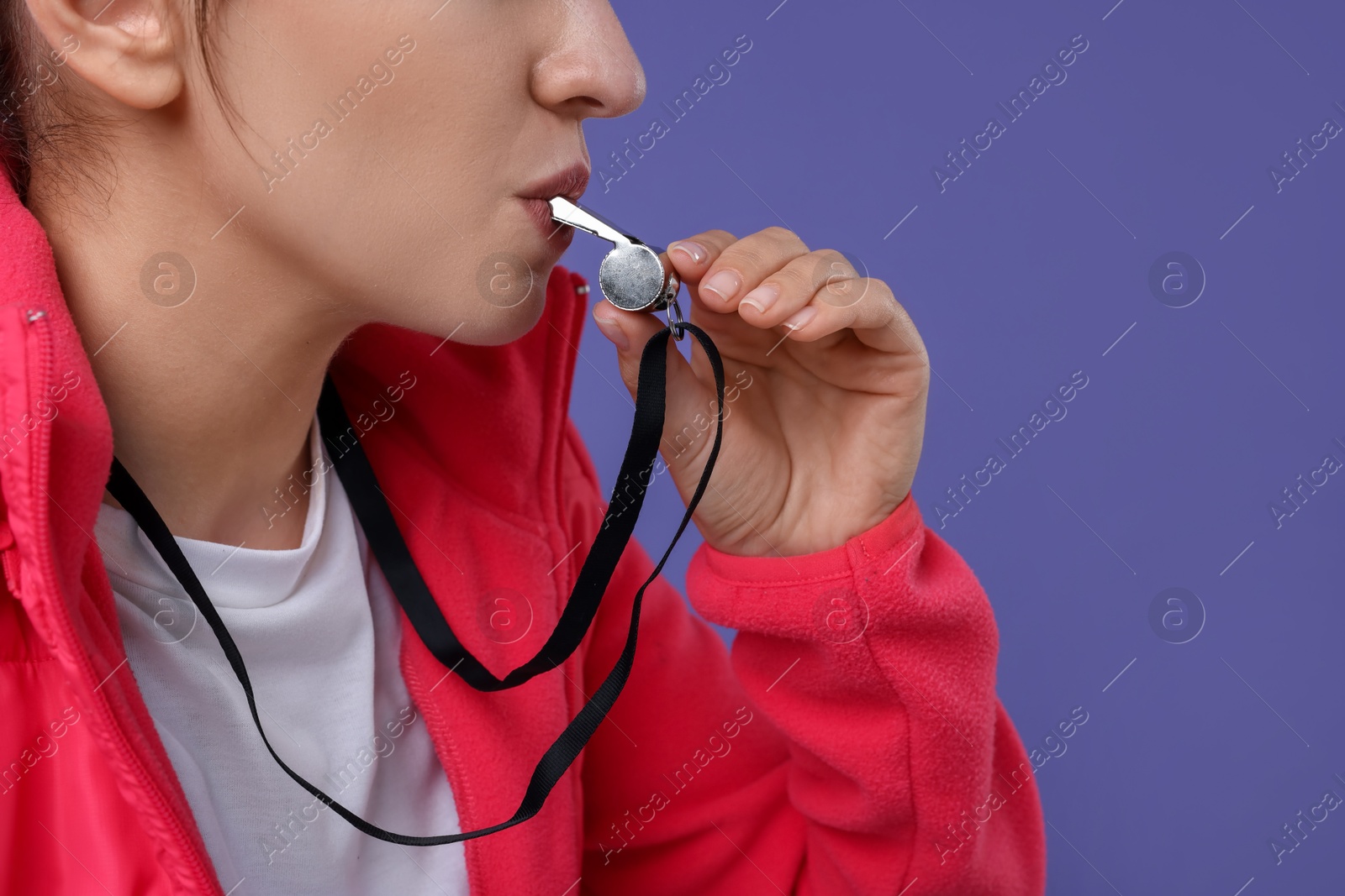 Photo of Woman blowing whistle on purple background, closeup