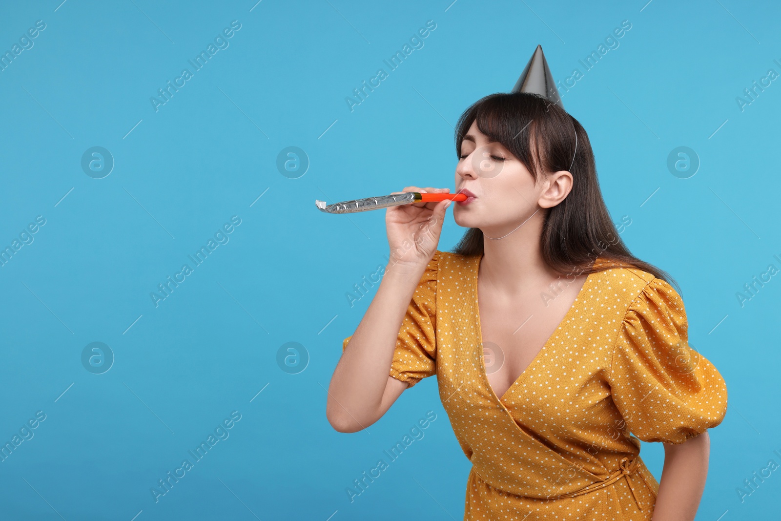 Photo of Woman in party hat with blower on light blue background, space for text