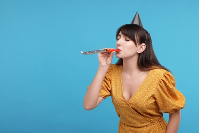 Woman in party hat with blower on light blue background, space for text