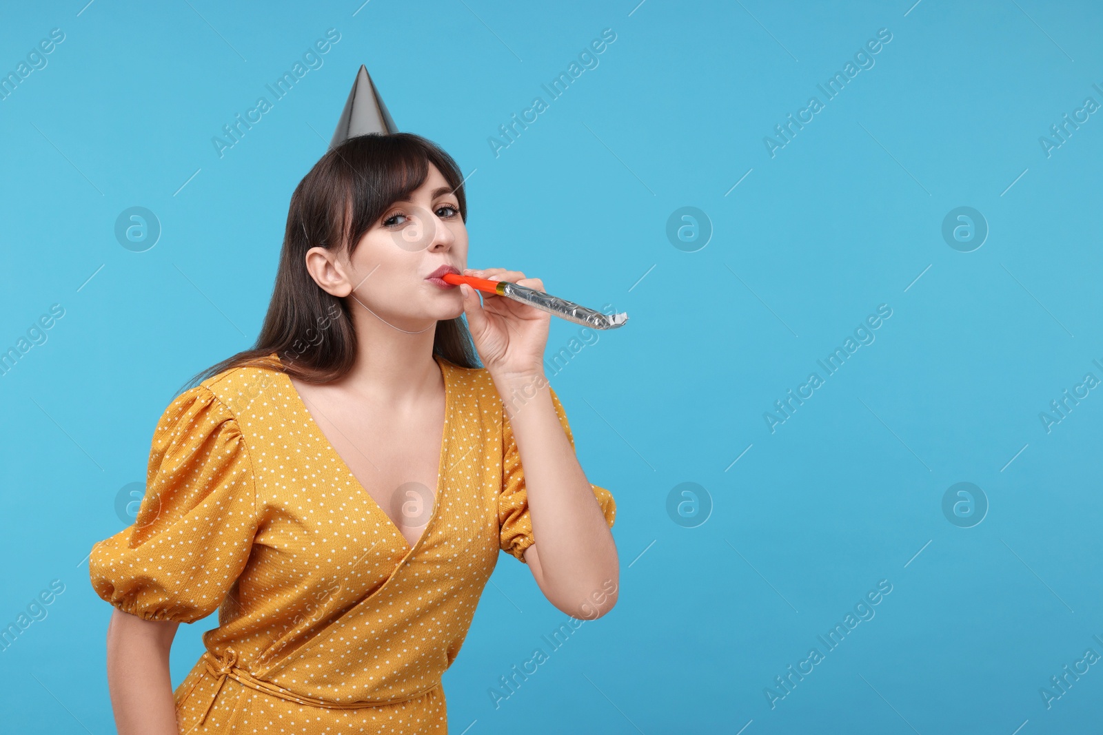 Photo of Woman in party hat with blower on light blue background, space for text