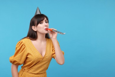 Woman in party hat with blower on light blue background, space for text