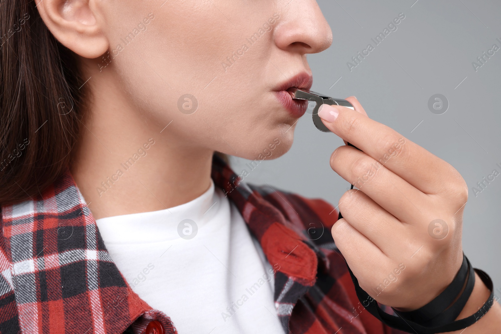 Photo of Woman blowing whistle on grey background, closeup