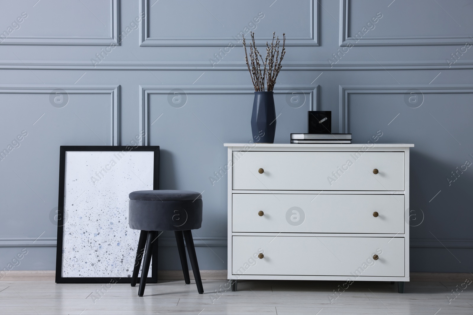 Photo of Stylish interior with stool and chest of drawers near light grey wall