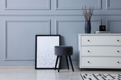 Photo of Stylish interior with stool and chest of drawers near light grey wall