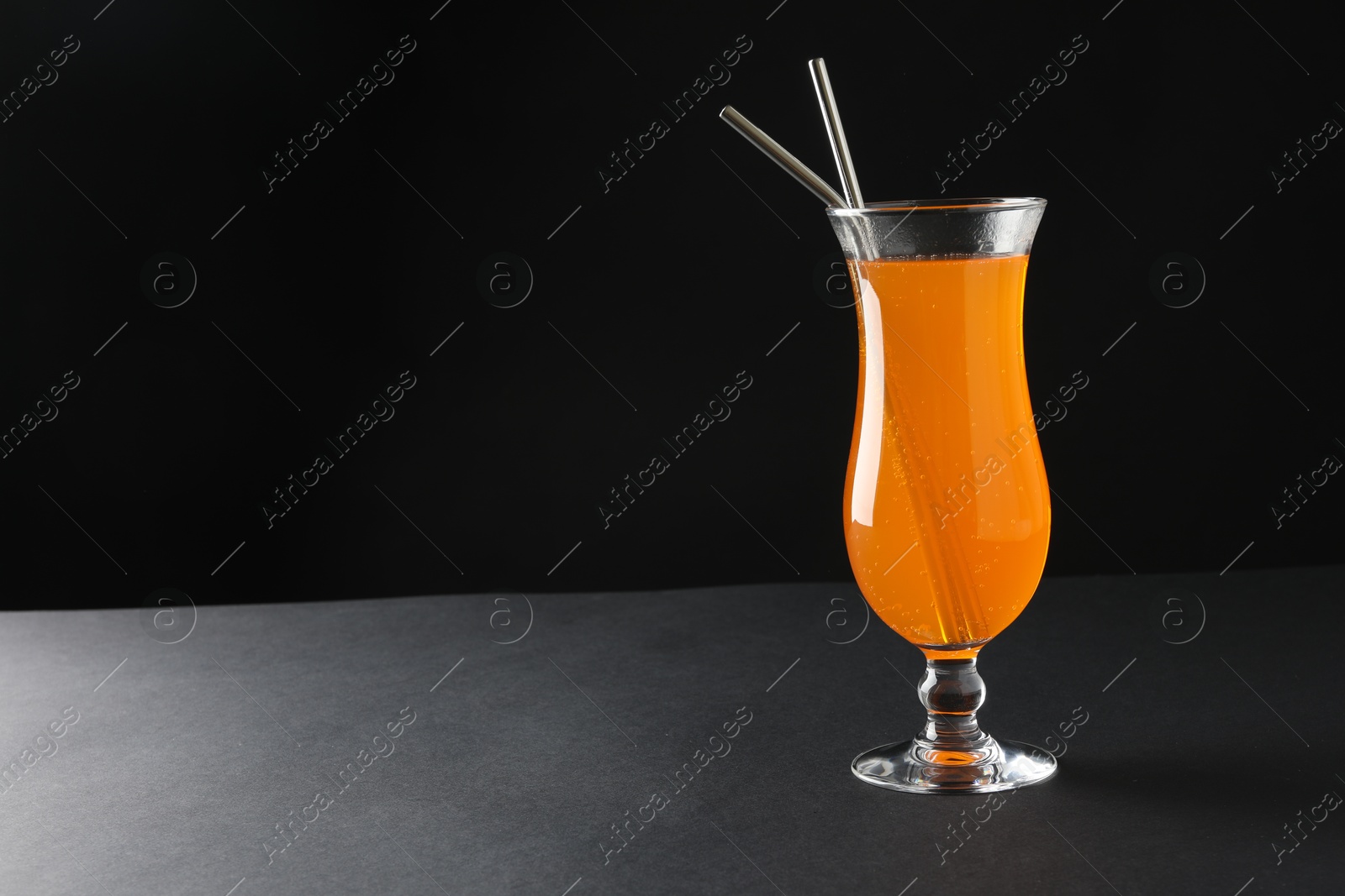 Photo of Tasty refreshing drink with straws in glass on grey table, space for text