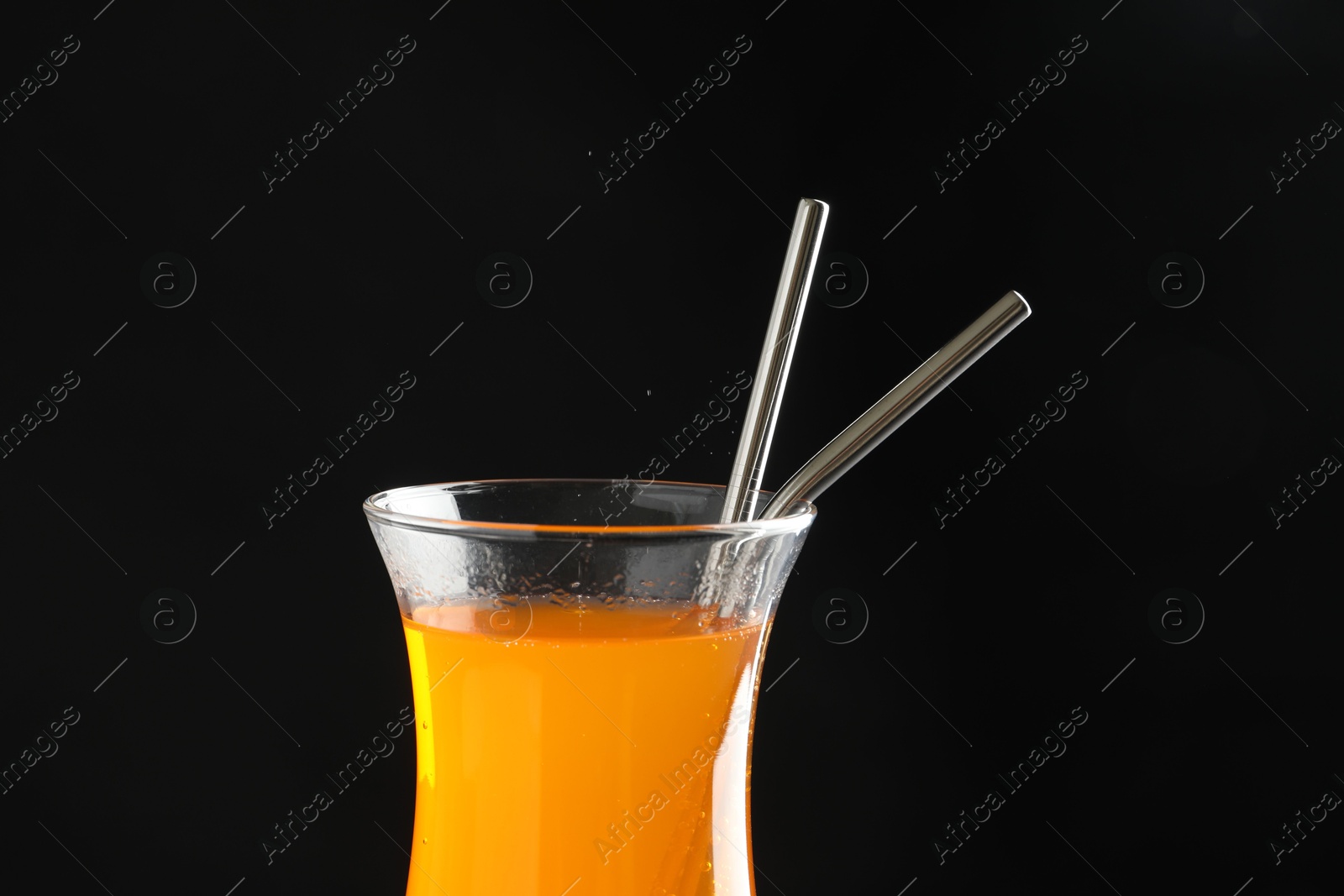 Photo of Tasty refreshing drink with straws in glass on black background, closeup