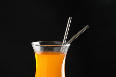 Photo of Tasty refreshing drink with straws in glass on black background, closeup