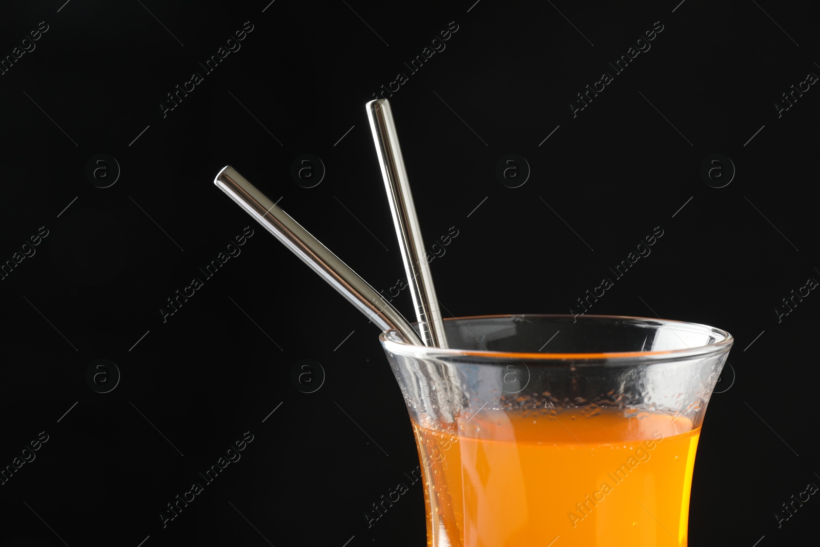 Photo of Tasty refreshing drink with straws in glass on black background, closeup