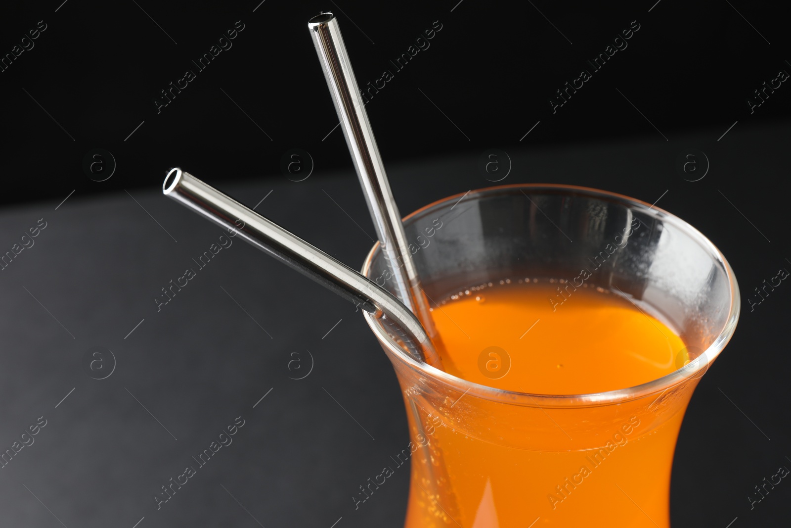 Photo of Tasty refreshing drink with straws in glass on dark background, closeup